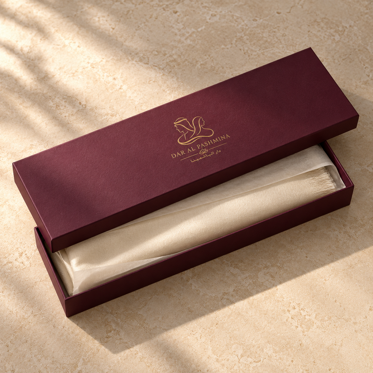 Presentation concept: plum-burgundy Dar Al Pashmina box with gold branding, ivory tissue and a folded shawl